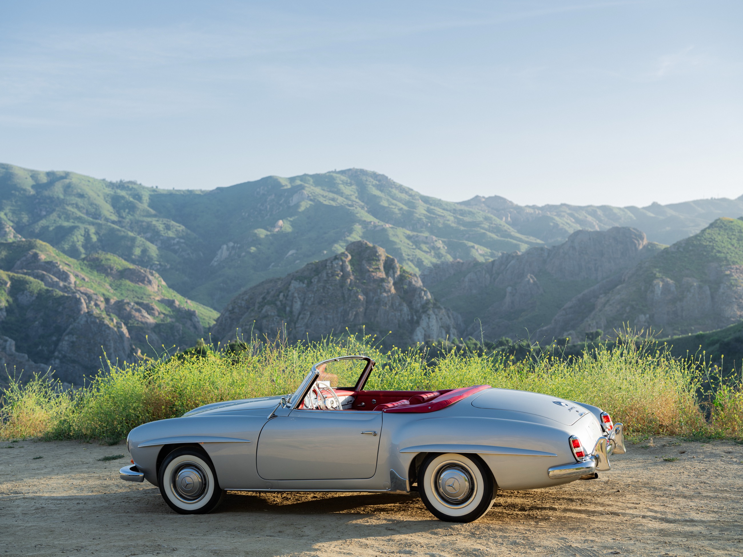Silver 1959 Mercedes-Benz 190 SL roadster with red leather interior parked above the Malibu canyons at golden hour