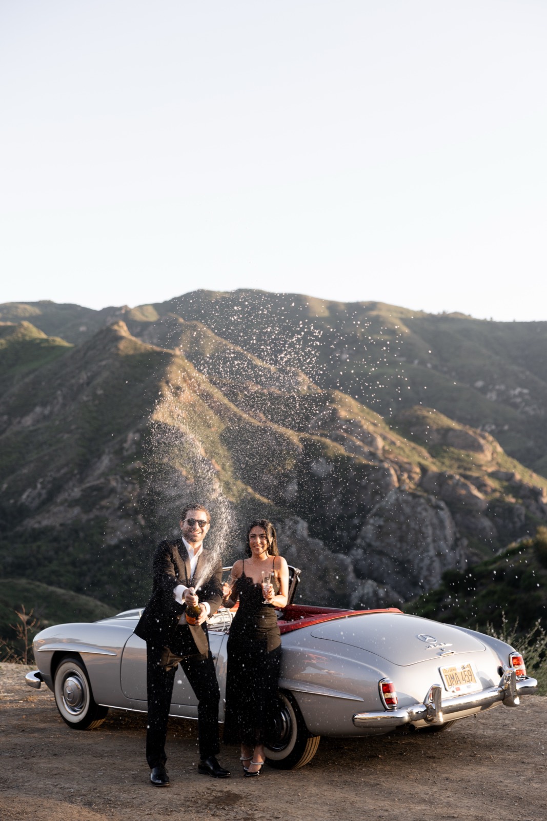 Couple spraying champagne in front of the 1959 Mercedes 190 SL in the Malibu canyons
